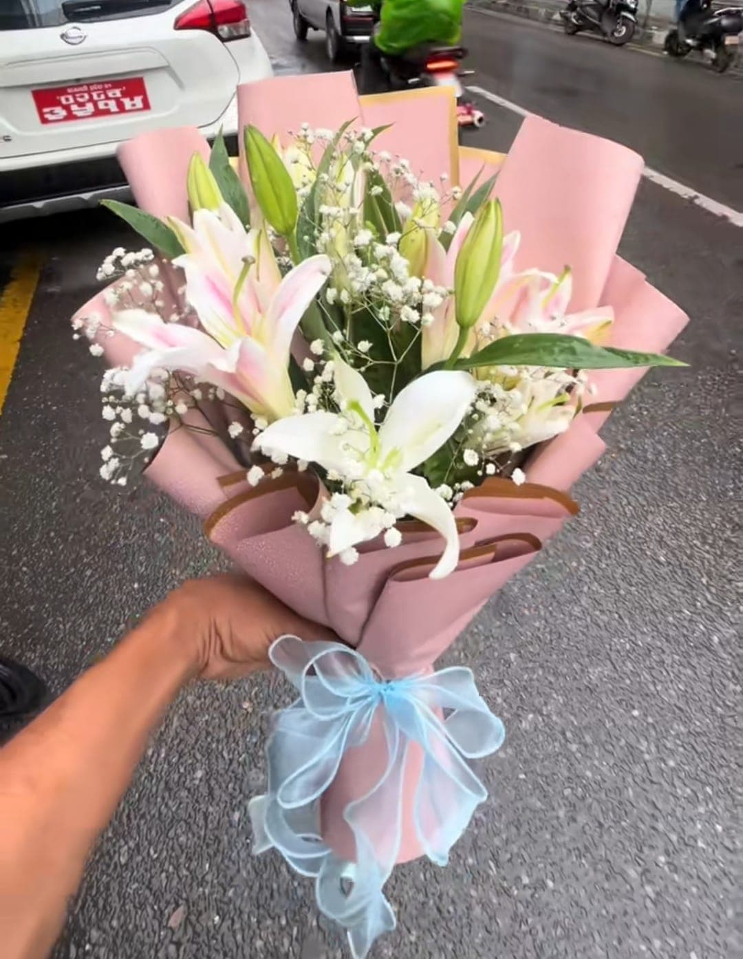 White lily bouquet with pink wrapping and a blue ribbon